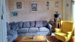 En stue med en grå sofa, en gul lænestol, et træsofabord og en trævæg med indrammede billeder.