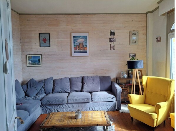 A living room with a grey sofa, a yellow armchair, a wooden coffee table, and a wooden wall with framed pictures.