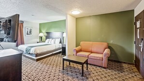A hotel room with a bed, a sofa, a small table, and a television. - Coratel Plus Luxury Suite 1 King bed with Sofa Non-Smoking Oversized (Wichita)