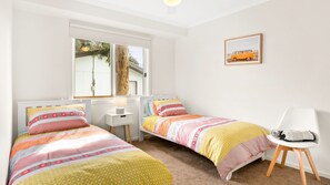 Quarto com duas camas de solteiro, uma mesinha de cabeceira com abajur, uma cadeira e janela com vista para árvores.