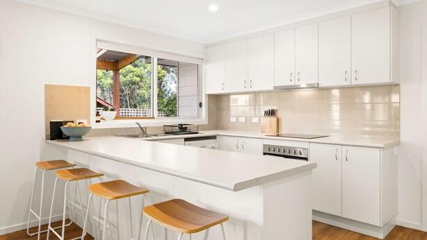 A modern kitchen with white cabinetry, a large island with bar stools, and a window overlooking greenery. - Churchill House - in Cowes (Cowes)