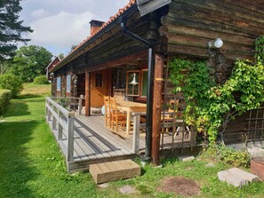 En rustik træhytte med træterrasse, udendørs møbler og en have.