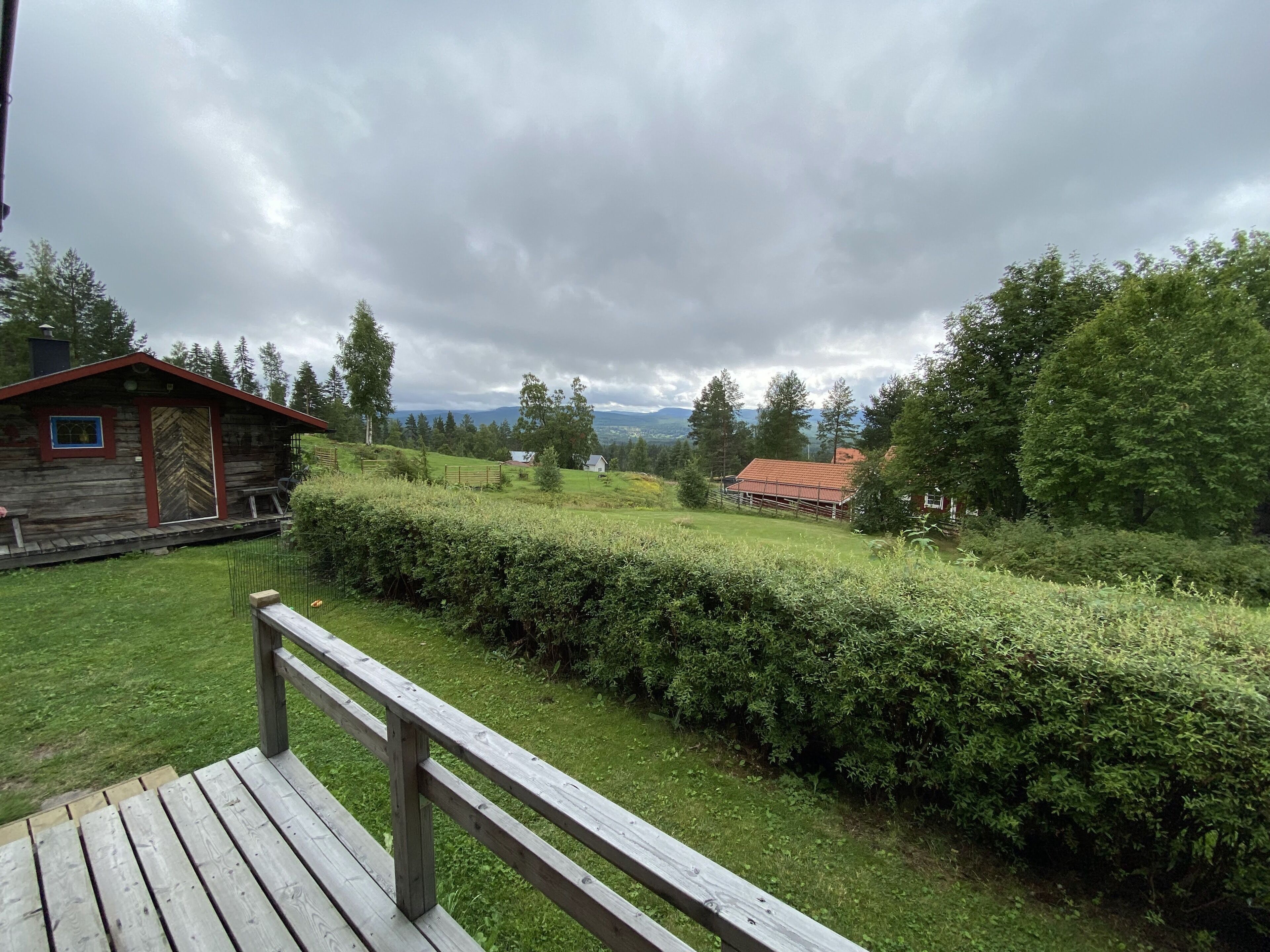 Puinen terassi, jolta avautuu näkymä maaseutumaisemaan, mukaan lukien puinen mökki ja punakattoinen rakennus.