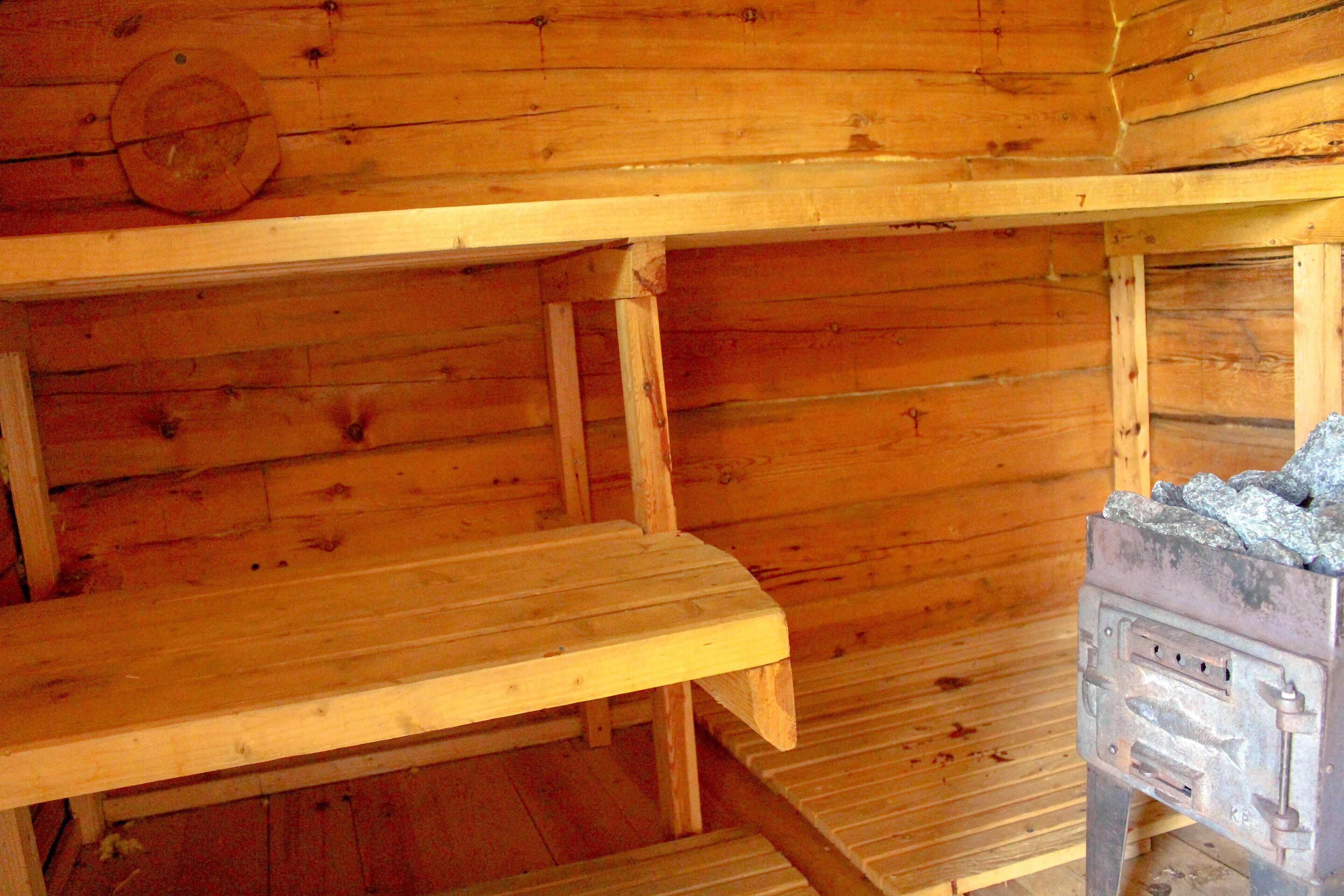 A wooden cabin interior with a metal stove, wooden benches, and a wooden wall with a circular window.