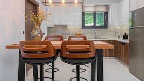 Een moderne keuken met witte kastjes, een houten eiland, twee barkrukken, een vaas met bloemen en een inbouwoven.