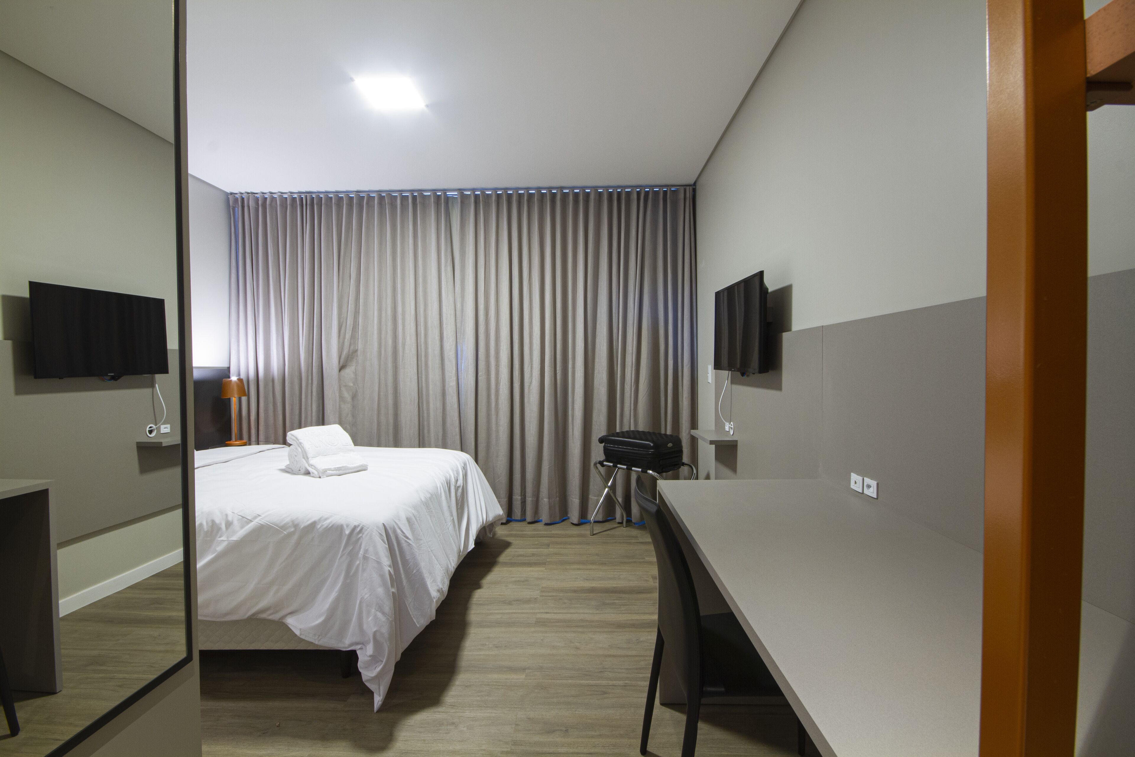 Une chambre d’hôtel avec un lit, un bureau, une chaise, une télévision et une fenêtre avec des rideaux.