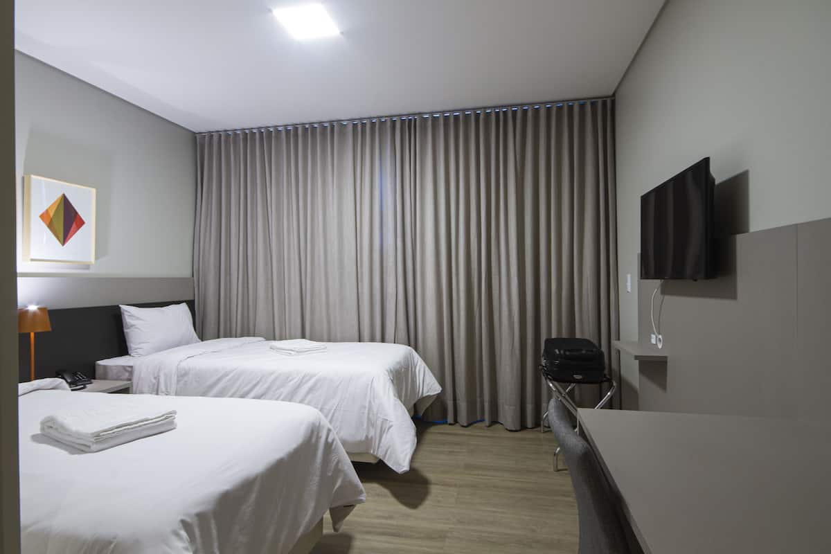 Habitación de hotel con dos camas, un escritorio, una silla, un televisor de pantalla plana y un ventanal grande con cortinas.