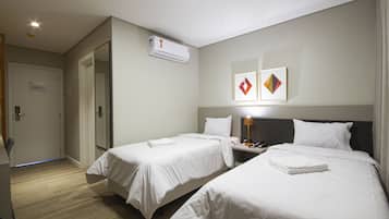 Una camera d'albergo con due letti, un comodino con una lampada, un condizionatore d'aria e una porta con un cartello.