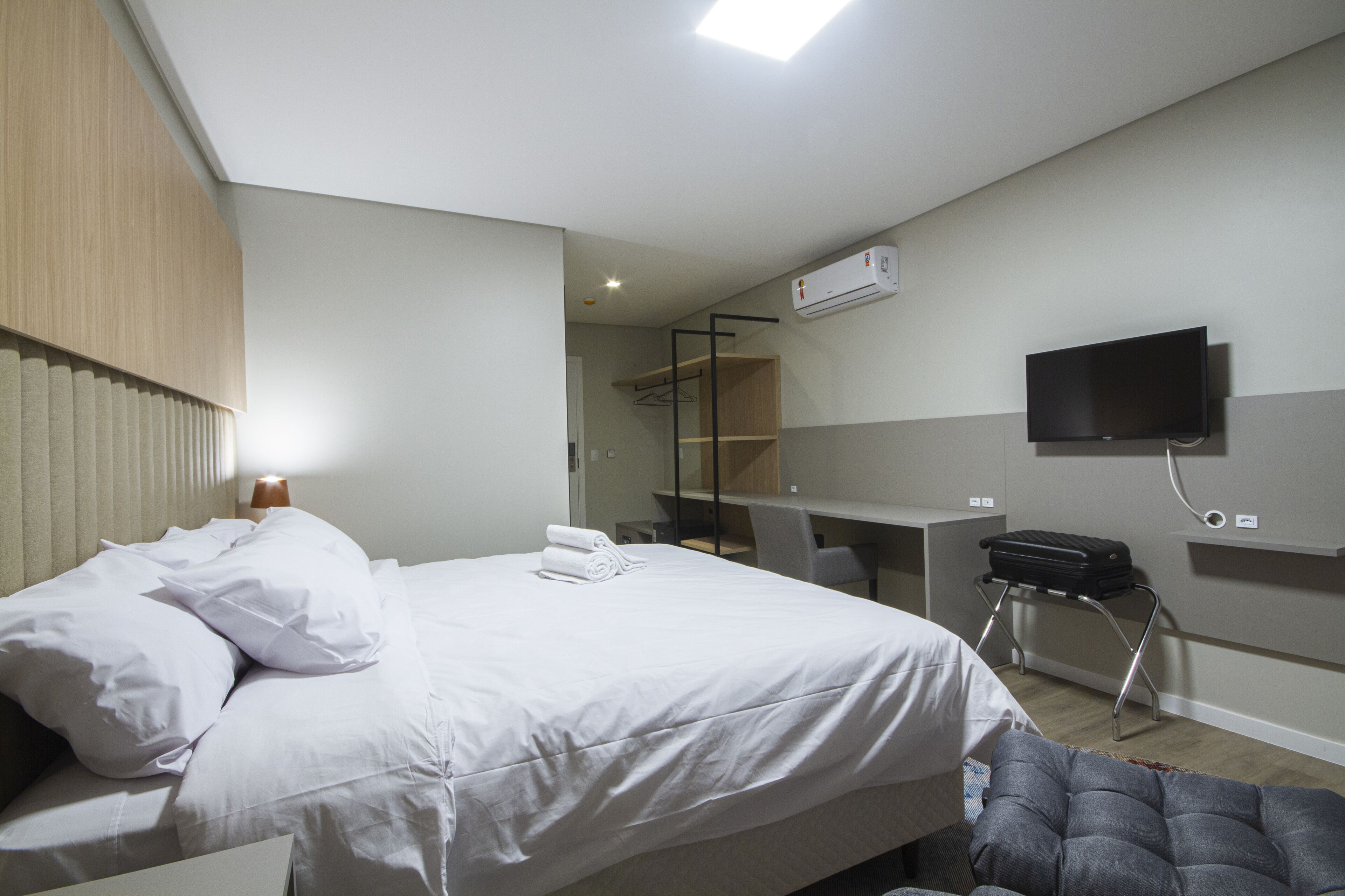 A hotel room with a bed, a desk, a chair, a TV, and a wardrobe.