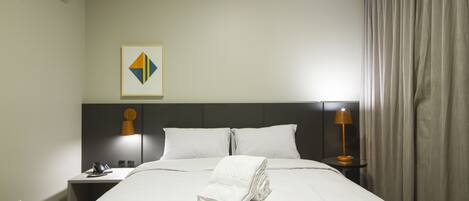 A hotel room with a neatly made bed, a nightstand with a lamp, a phone, and a wall-mounted air conditioner.