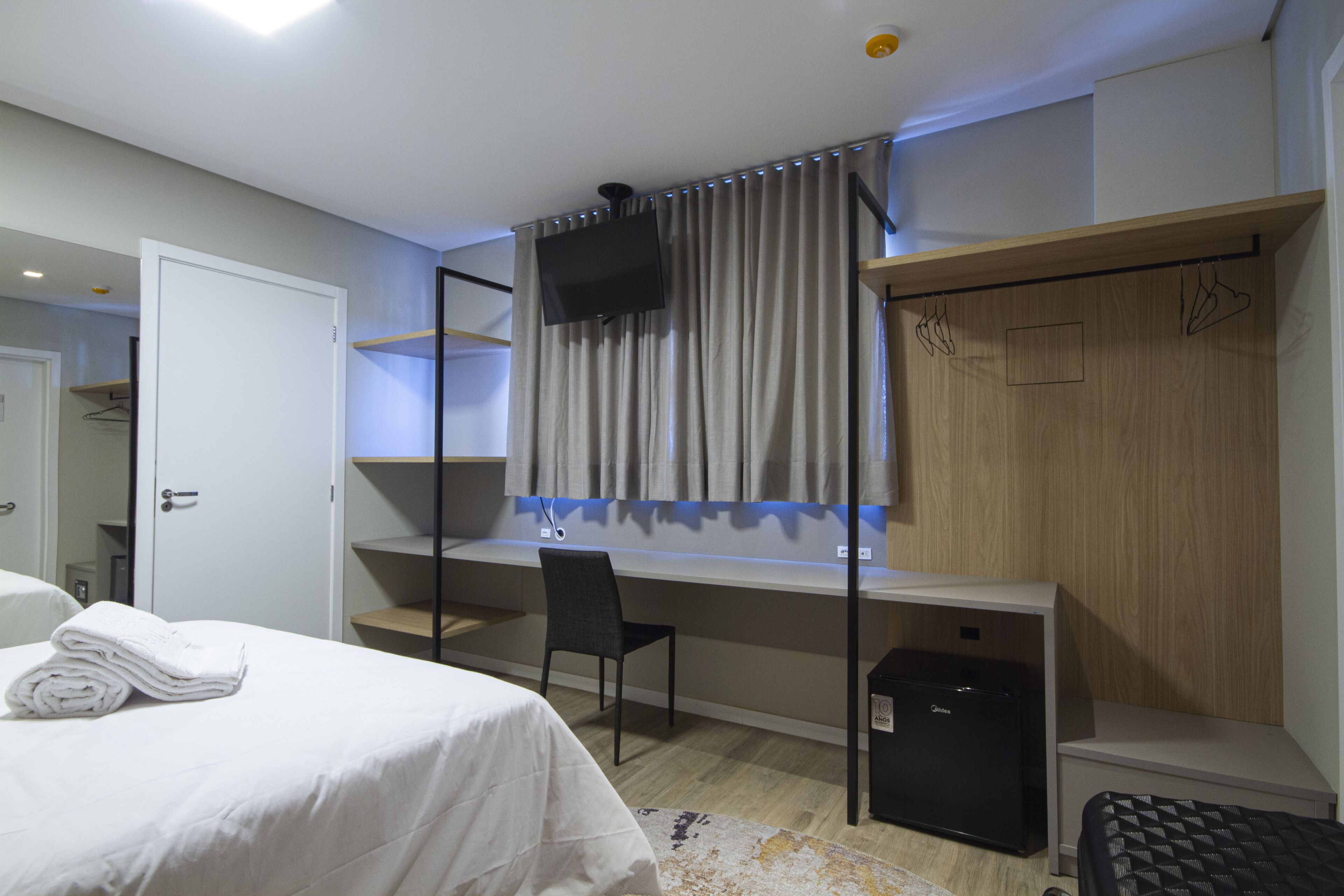 Een hotelkamer met een bed, een bureau, een stoel, een televisie en een garderobe.