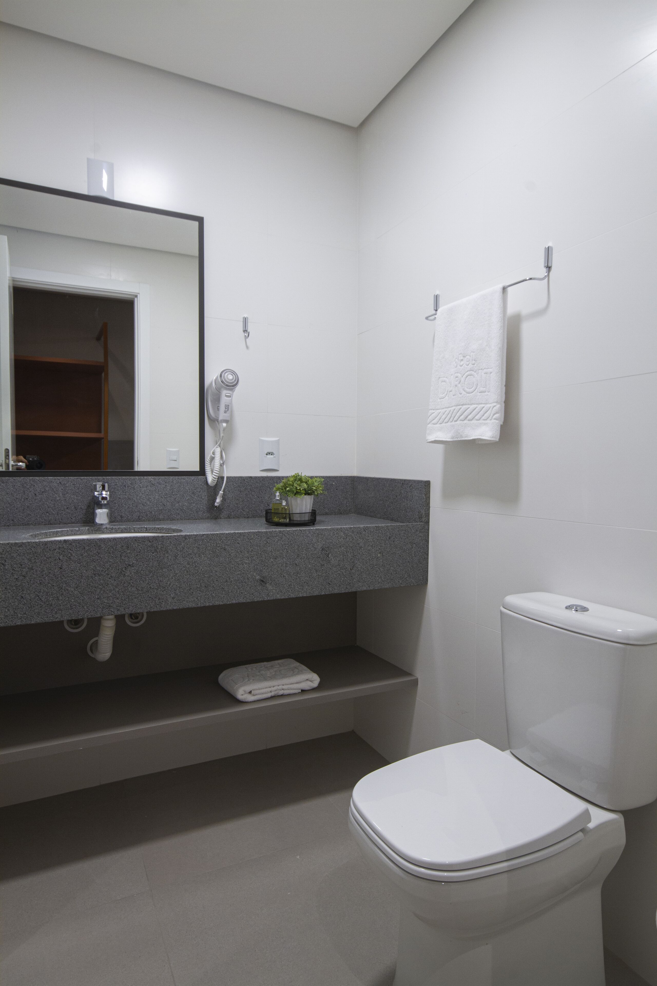 A modern bathroom with a white sink, a hairdryer, a towel, and a toilet.