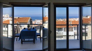 Ein Balkon mit Tisch und Stühlen, Blick auf das Meer und Gebäude.