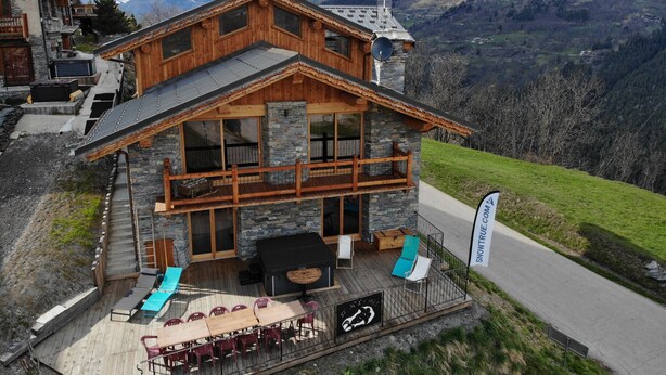 Eine Holzhütte mit Steinverkleidung, einem Balkon und einem Essbereich mit Gartenmöbeln.