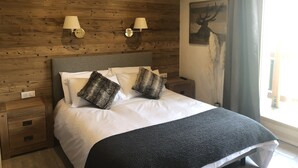Ein Schlafzimmer mit Holzwänden, einem Bett, zwei Wandlampen, einem Nachttisch und einem Bild von einem Reh.