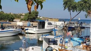 Un restaurante frente al agua con mesas y sillas, barcos amarrados al fondo y una vista despejada del agua.