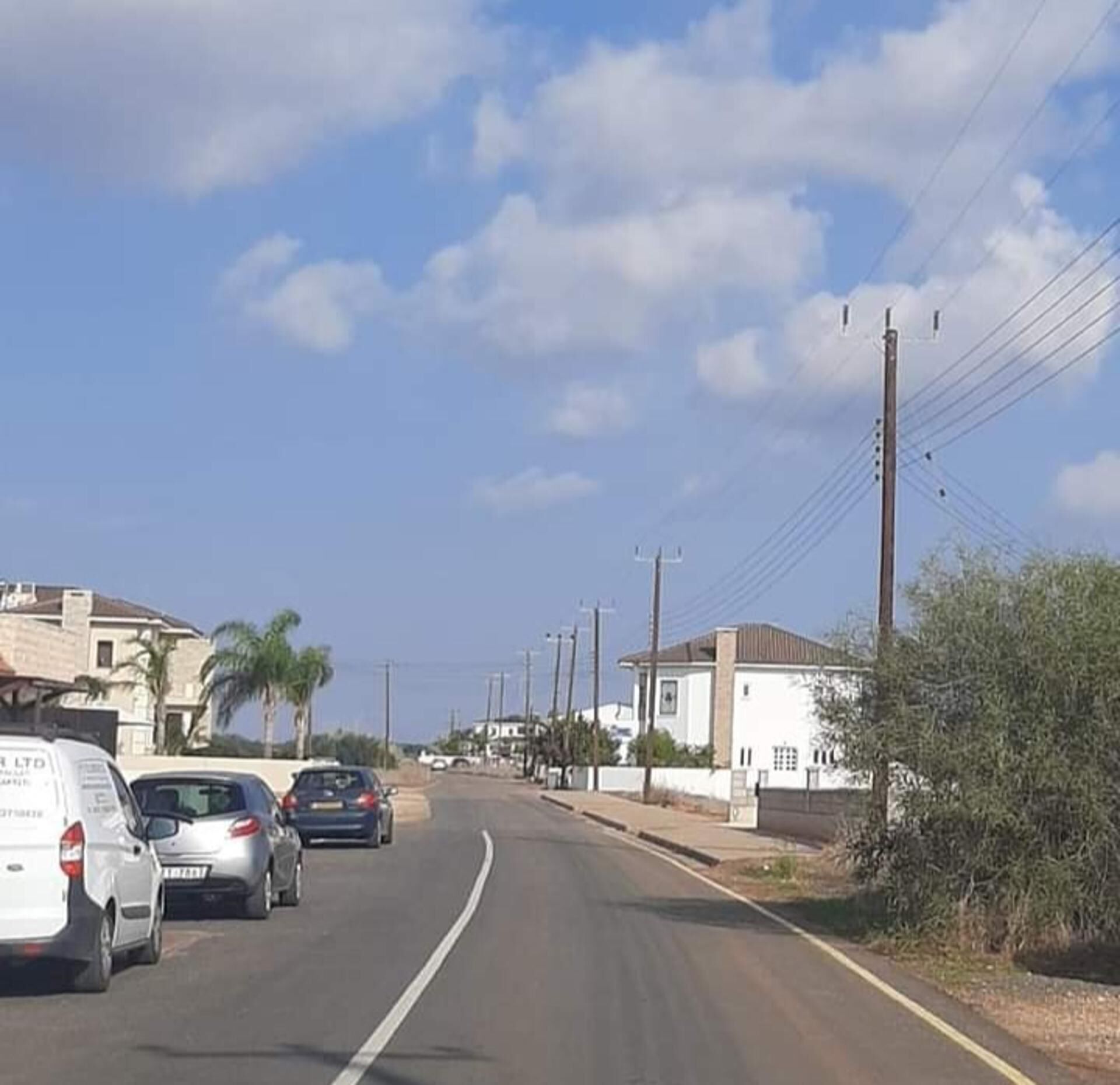 Una carretera con coches aparcados y casas a los lados.