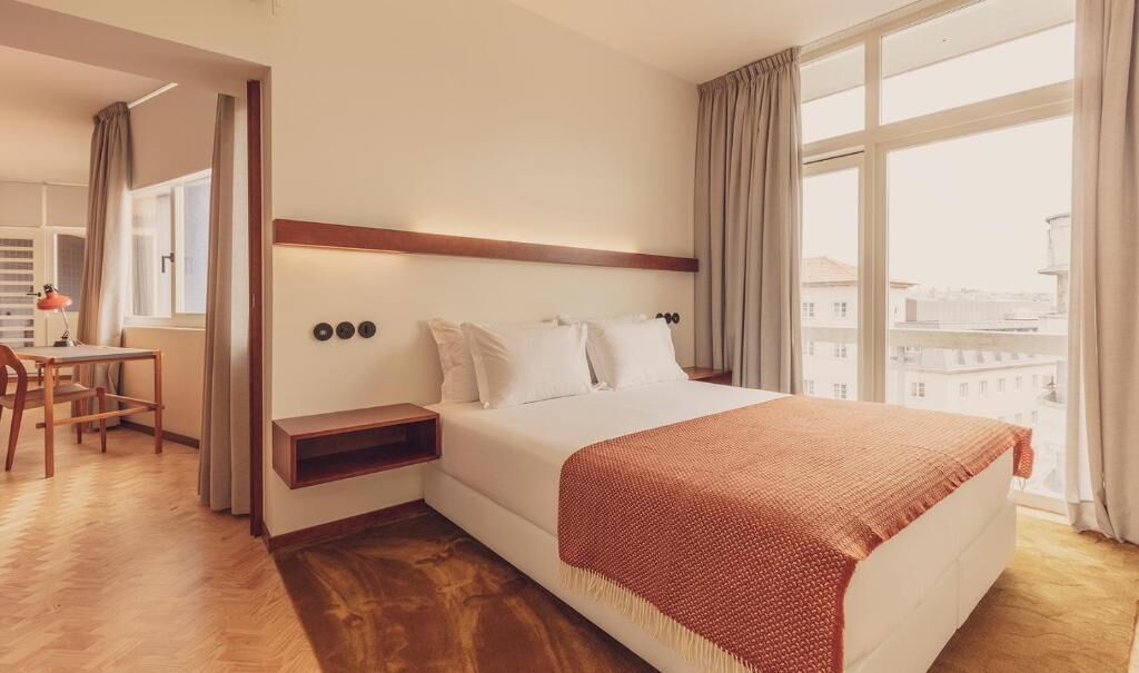 A hotel room with a bed, a desk, and a view of the city.