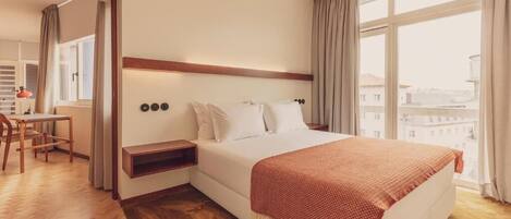 A hotel room with a bed, a desk, and a view of the city.