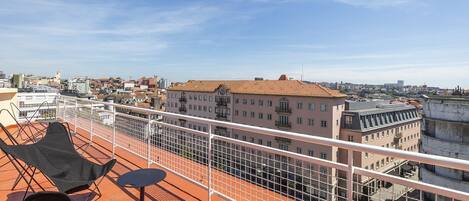 Terraza en la azotea con vista a un paisaje urbano, que incluye una barandilla y dos sillas.