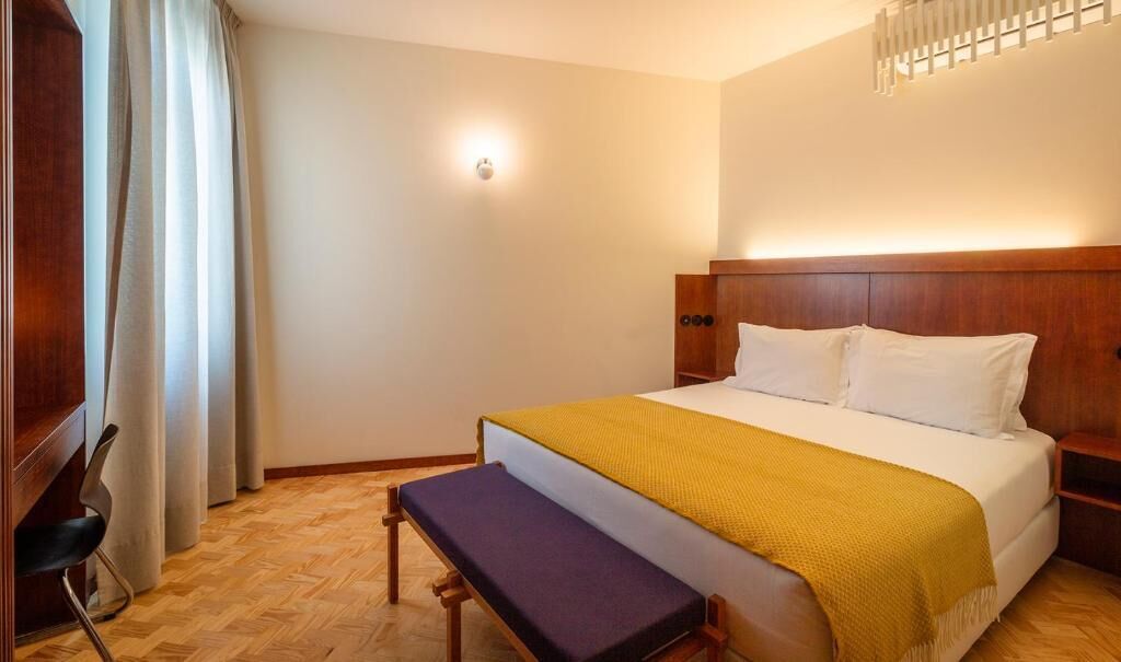 A neatly arranged bedroom with a bed, bench, and a wall-mounted light fixture.