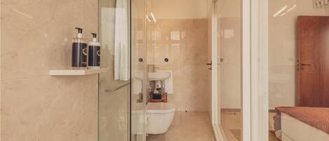 A modern bathroom with a glass shower enclosure, a white sink, and a wooden door.