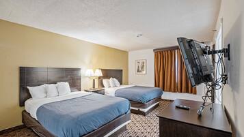 Habitación de hotel con dos camas, televisión, escritorio y alfombra estampada.