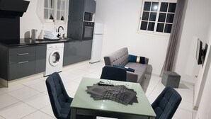 A compact kitchen with modern appliances, a dining area with a table and chairs, and a grey sofa. - The Island Paradise (Baillif)