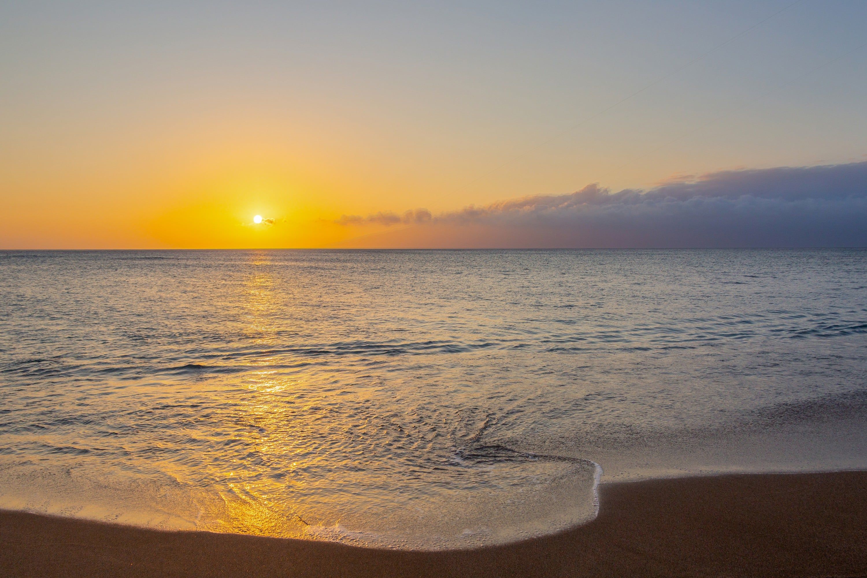 Una playa con el sol poniéndose sobre el océano, creando un ambiente tranquilo y sereno.