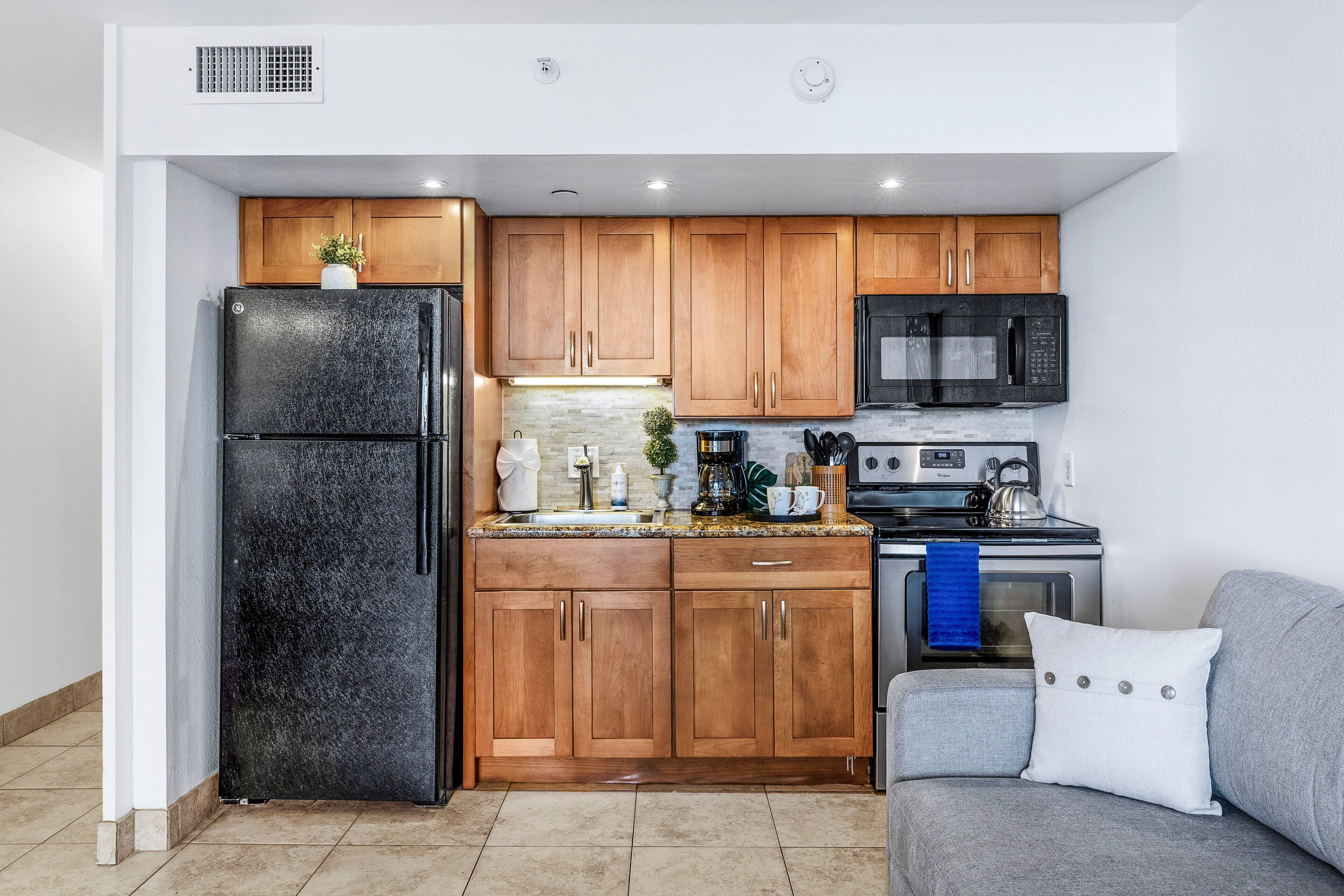 Una cocina compacta con armarios de madera, un refrigerador negro, un microondas y una estufa.
