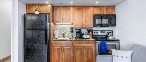 Una cocina compacta con armarios de madera, un refrigerador negro, un microondas y una estufa.