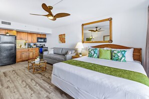 A hotel room with a bed, a sofa, a kitchen area, and a ceiling fan.