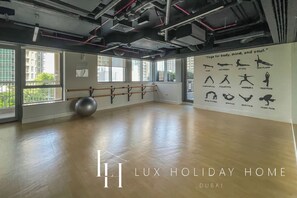 A spacious yoga studio with a wooden floor, large windows, and a wall with yoga poses illustrated. - LUX The Downtown Blvd Suite (Dubai)
