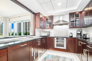 A modern kitchen with dark wood cabinets, stainless steel appliances, and a large window offering a city view. - LUX The Downtown Blvd Suite (Dubai)