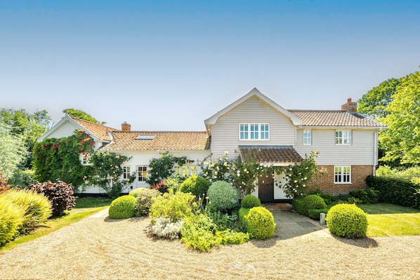 A two-story house with a tiled roof, surrounded by a well-maintained garden with various shrubs and flowers.
