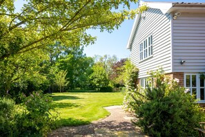 A well-maintained garden with a brick pathway leading to a house with white siding and a brick foundation.