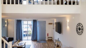A modern living room with a sofa, coffee table, and a dining table. There is a staircase leading to an upper level. - Coverack (Falmouth)
