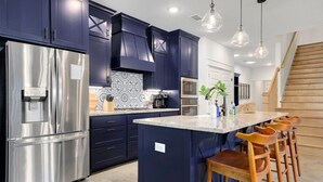 Una cocina moderna con armarios azul oscuro, electrodomésticos de acero inoxidable y una isla central con taburetes de bar.