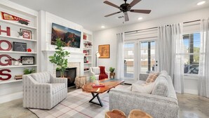 Una sala de estar moderna con chimenea, ventilador de techo y un ventanal con cortinas.