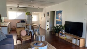 Ein modernes Wohnzimmer mit Flachbildfernseher, einem Essbereich mit Tisch und Stühlen sowie einer Küche im Hintergrund.