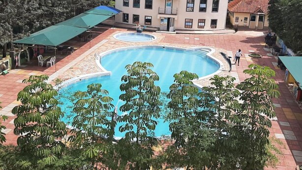 A swimming pool with a unique shape, surrounded by a building with a red roof and multiple windows. - Three Rivers Resort Maragua (Nairobi)