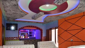 A room with white upholstered chairs, a TV mounted on the wall, and a colorful ceiling design. - Three Rivers Resort Maragua (Nairobi)