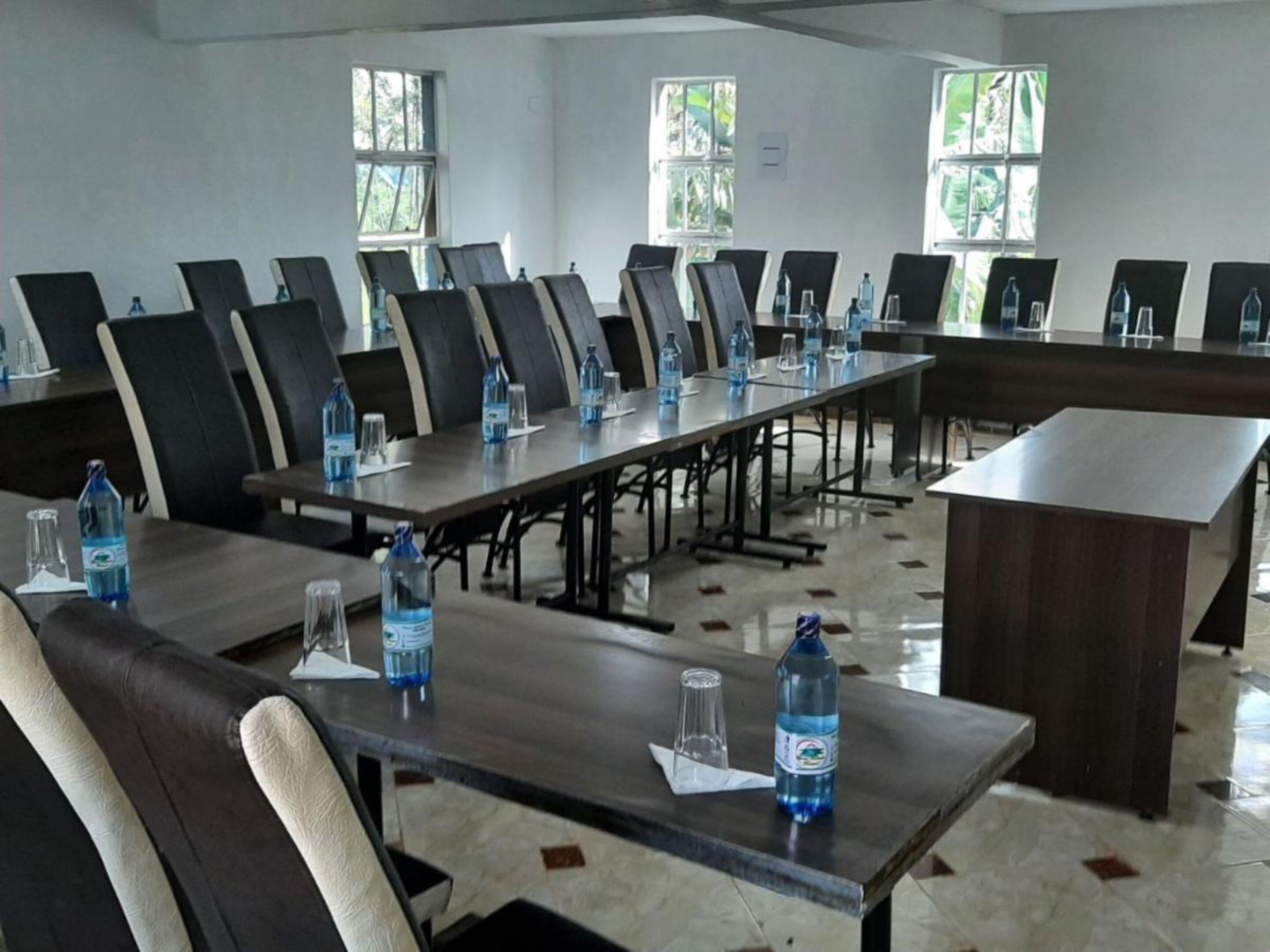 A conference room with multiple tables and chairs, water bottles on tables, and windows with natural light.