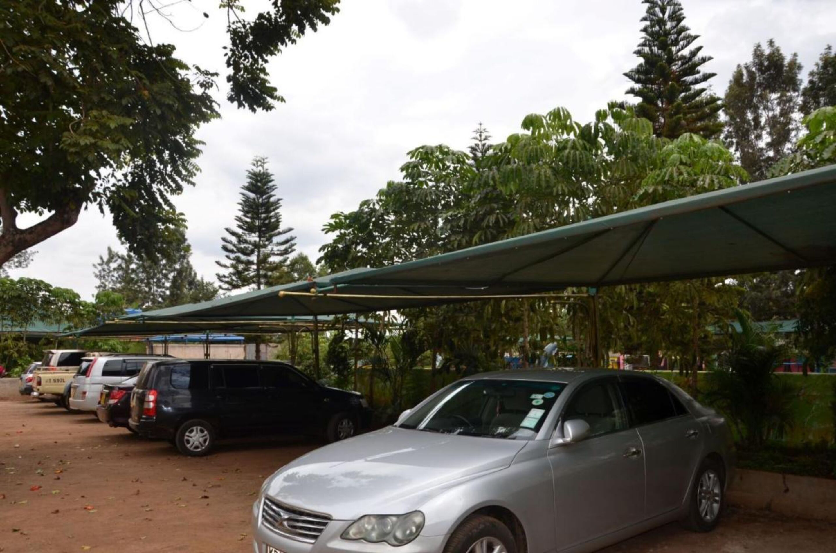 A parking area with several cars, a covered shelter, and trees in the background.