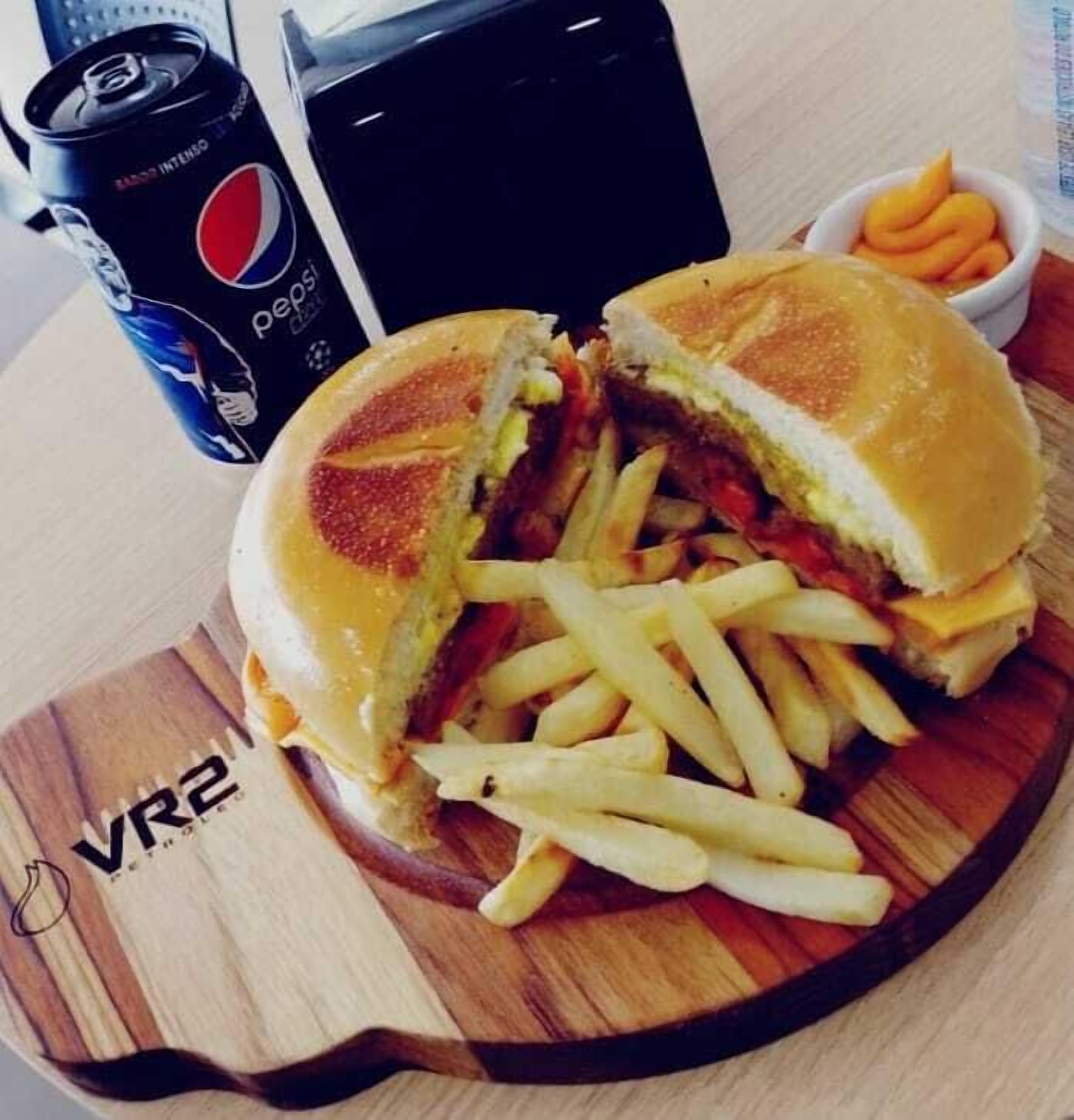 Un sándwich cortado por la mitad, sobre una tabla de madera con papas fritas y una bebida al lado.