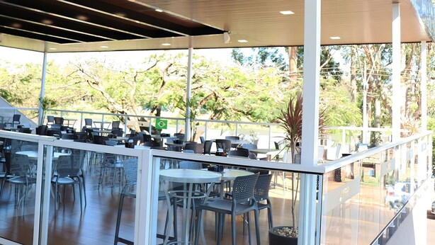 An outdoor café with tables and chairs, a wooden canopy, and a view of trees and a road. - VR2 Hotel (Lencois Paulista)