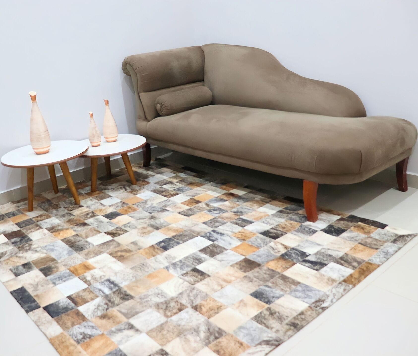A beige sofa, a small round table with three vases, and a patterned rug.