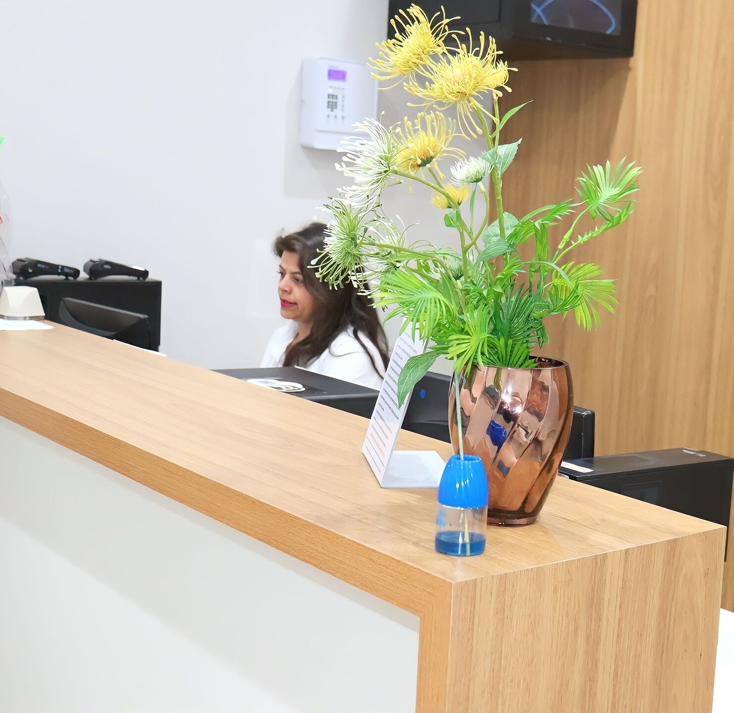 Una recepción con un jarrón de flores, un termostato digital y un televisor montado en la pared.