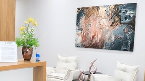 A reception area with a wooden desk, a vase of flowers, a blue lamp, and a painting on the wall. - VR2 Hotel (Lencois Paulista)