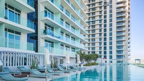 A modern hotel with a pool area, multiple balconies, and a clear view of the surrounding buildings. - Maison Privee - Sunrise Bay Tower 2 (Dubai)